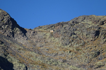 Observamos, muy pequeño, dominando el circo del Pla del Estany desde las alturas, el refugio de madera de los Estanys Forcats.