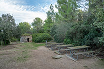 Zona de descanso con mesas, bancos y una barraca de piedra seca.