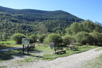 Área de picnic con mesas, bancos y un panel interpretativo.