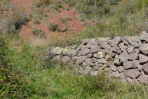 Murete de piedras con la señal amarilla del sendero que debemos tomar.